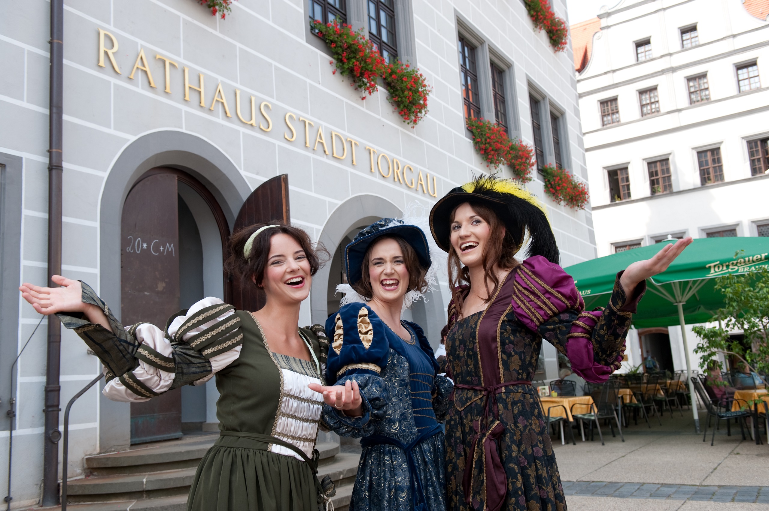 Drei Frauen in Renaissance-Kleidung stehen vor dem Rathaus in Torgau. 