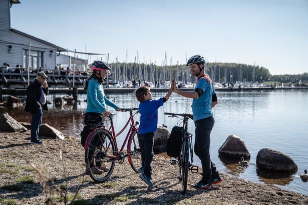 Eine Familie steht mit ihren Rädern am Cospudener See, Vater und Sohn geben sich ein High Five.