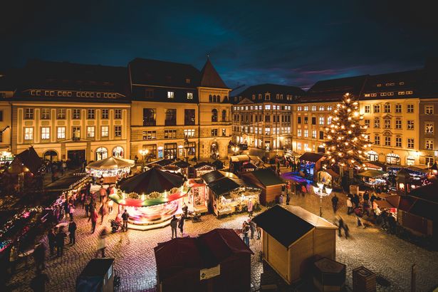View over the Christmas market in Bautzen during the evening with loads of decorating lights around the market stalls, a large christmas tree and a carousel