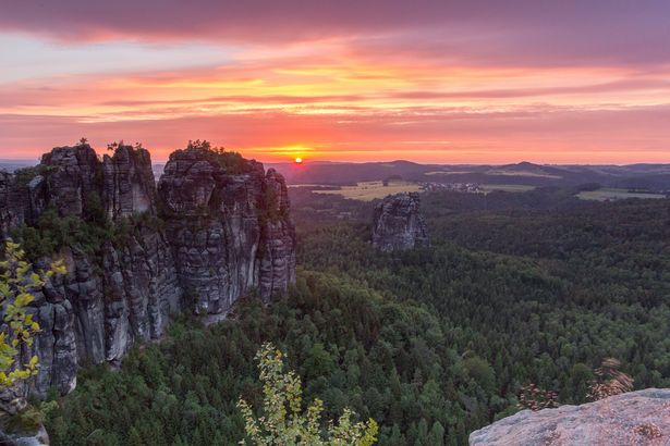 Links erheben sich die Schrammsteine im Nationalpark Sächsische Schweiz. Dahinter geht die Sonne unter.